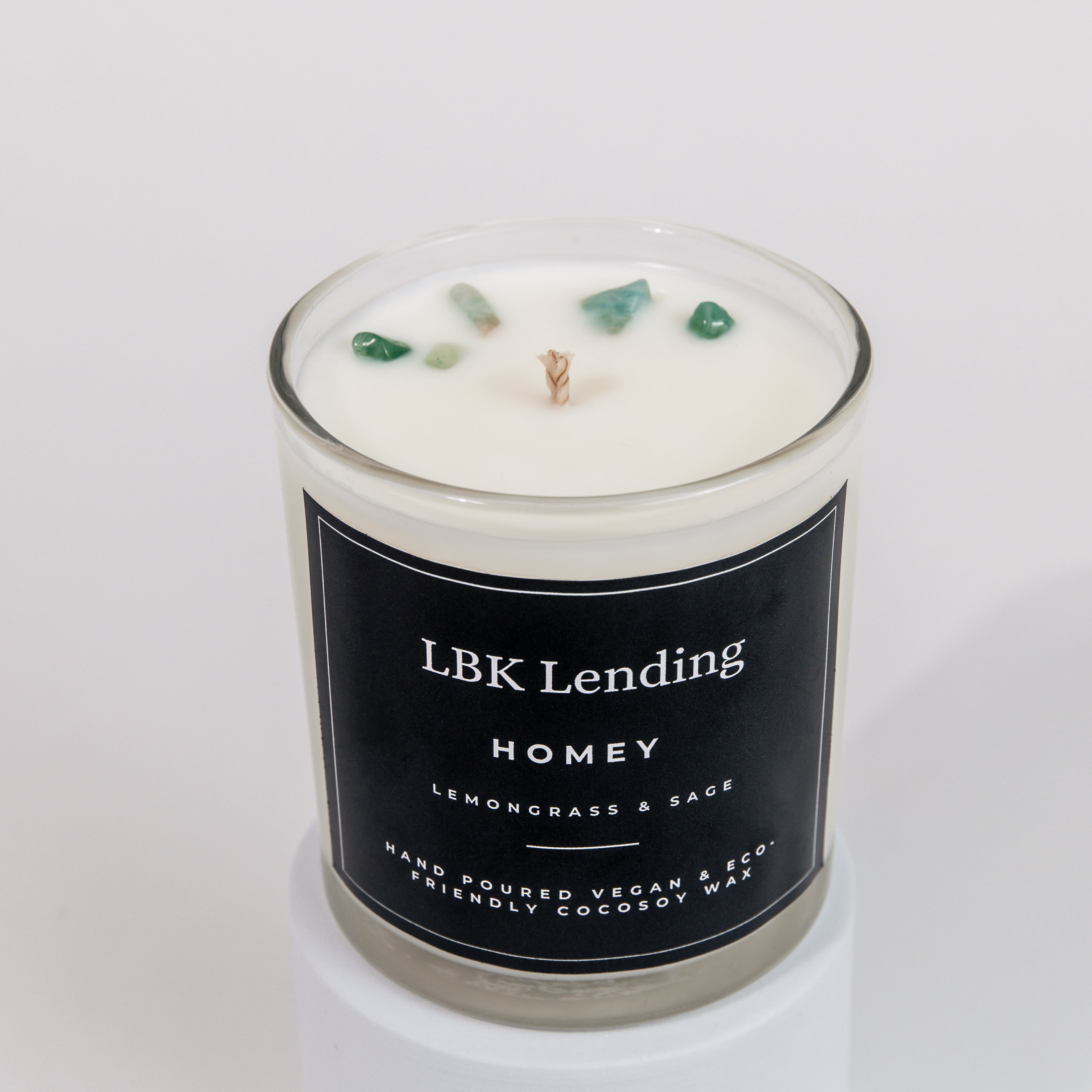 A white cocosoy wax candle in a clear glass jar with a black label reading 'LBK Lending HOMEY Lemongrass & Sage'. The candle is topped with three small green crystals and a single wick, set against a clean white background.