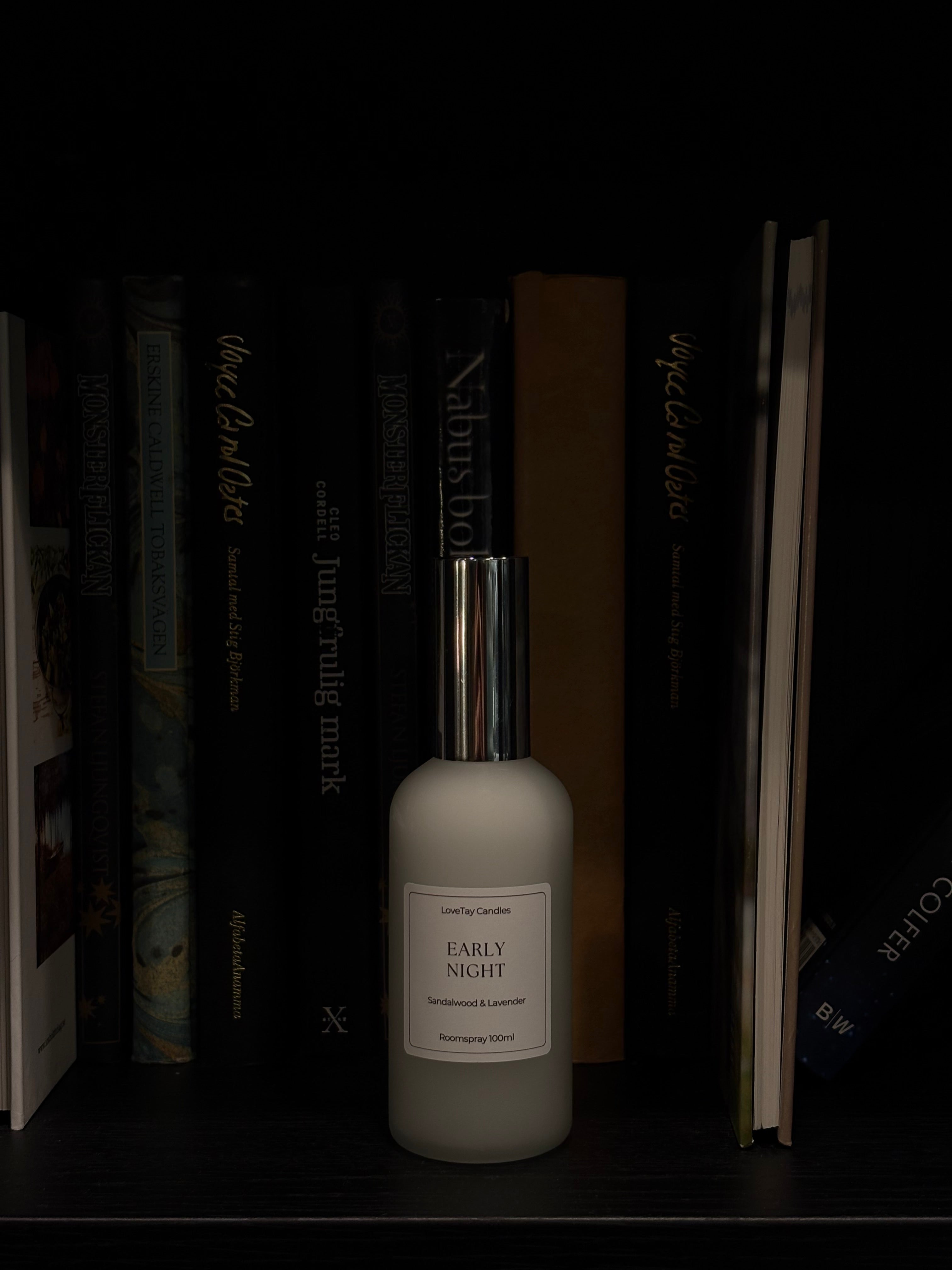 A frosted glass bottle of 'Early Night' body wash by 'LoveTay Candles' with a metallic silver cap, displayed on a dark bookshelf between books.
