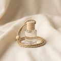 A clear glass reed diffuser bottle with a stacked wooden top and a braided beige rope loop, resting on soft cream fabric.