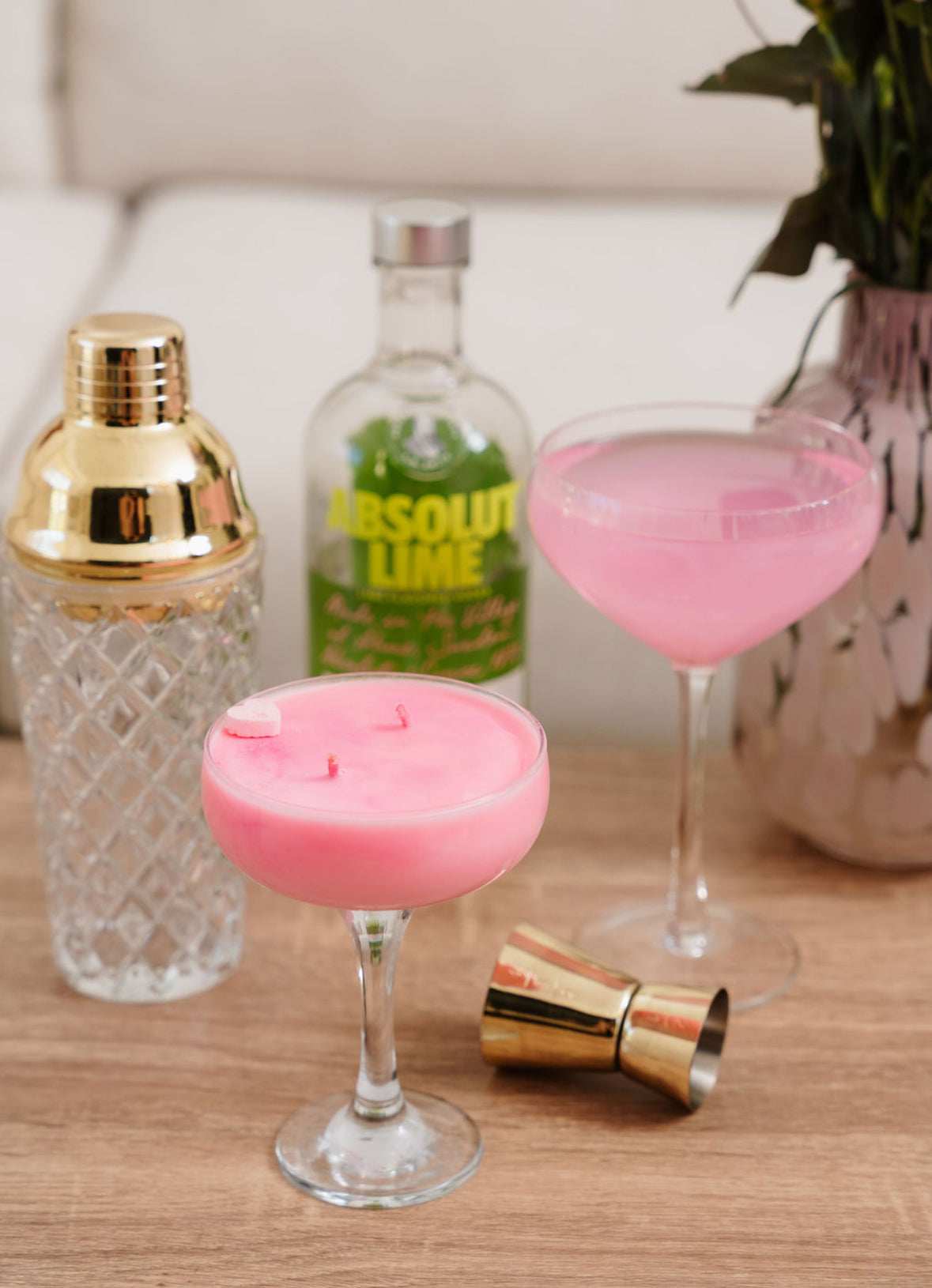 Pink LoveTay Cocktail Candle with a pink cocktails in coupes with a bottle of Absolut Lime vodka on a wooden surface